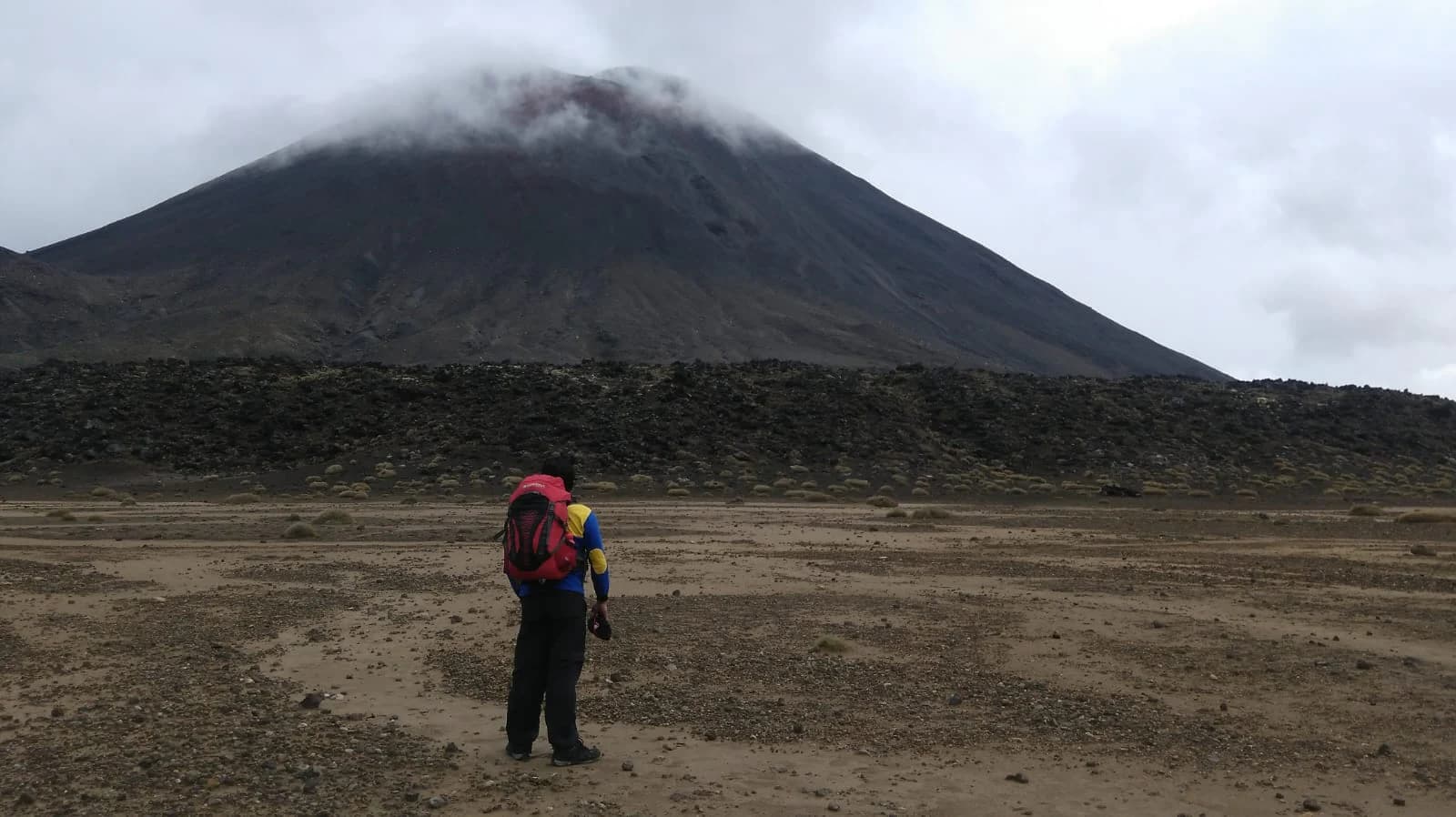 A field figure viewing a large volcanic cone across a barren plain