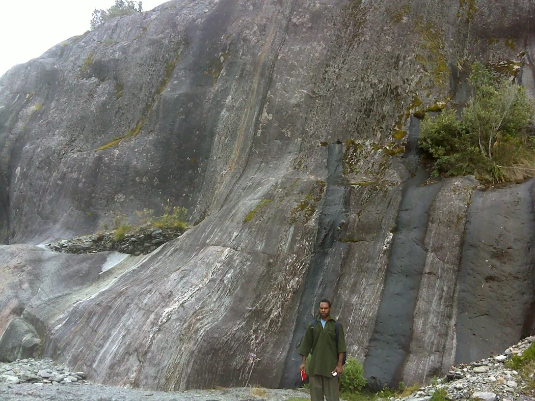 A person standing in front of a tall streaked rock face for scale