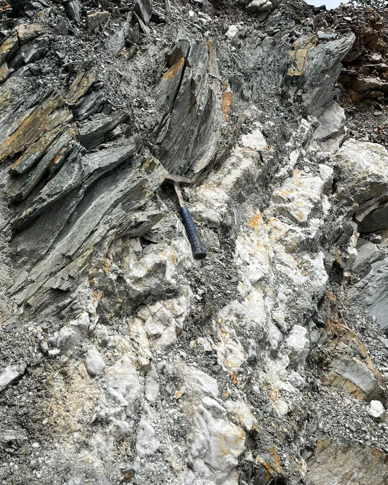 A geological hammer placed for scale across a pale vein cutting dark foliated rock
