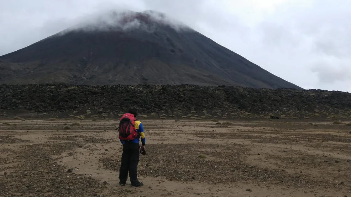 A field figure viewing a large volcanic cone across a barren plain